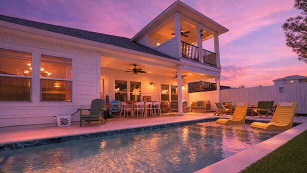 Una casa de dos pisos con un porche cubierto, piscina y mobiliario para exteriores.