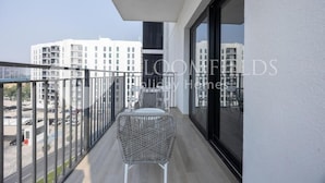 A balcony with a wicker chair and a table, overlooking a cityscape with modern buildings. - Bloomfields Unique 1BR Water's Edge2  (Abu Dhabi)