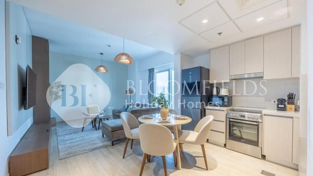A modern kitchen with built-in appliances, a dining area with a round table and chairs, and a living space with a sofa and a TV. - Bloomfields Unique 1BR Water's Edge2  (Abu Dhabi)