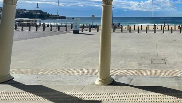 En täckt gångväg med kolonner som leder till ett område vid stranden med fri utsikt över havet.