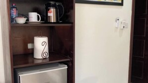Eine kleine Küchenzeile mit Kühlschrank, Kaffeemaschine und einer Rolle Küchenpapier auf einem Regal.