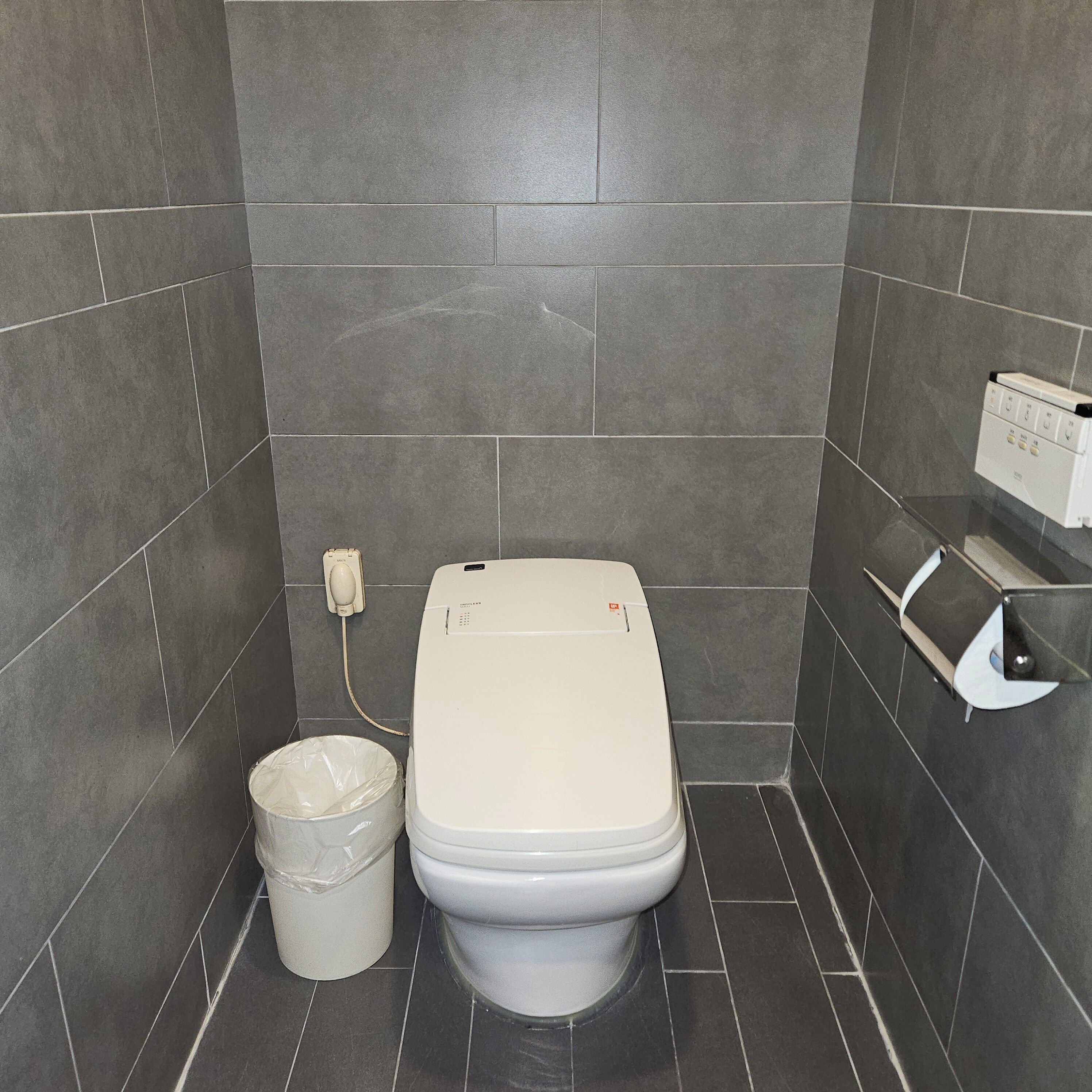 A small bathroom with a toilet, a trash bin, and a hand dryer.