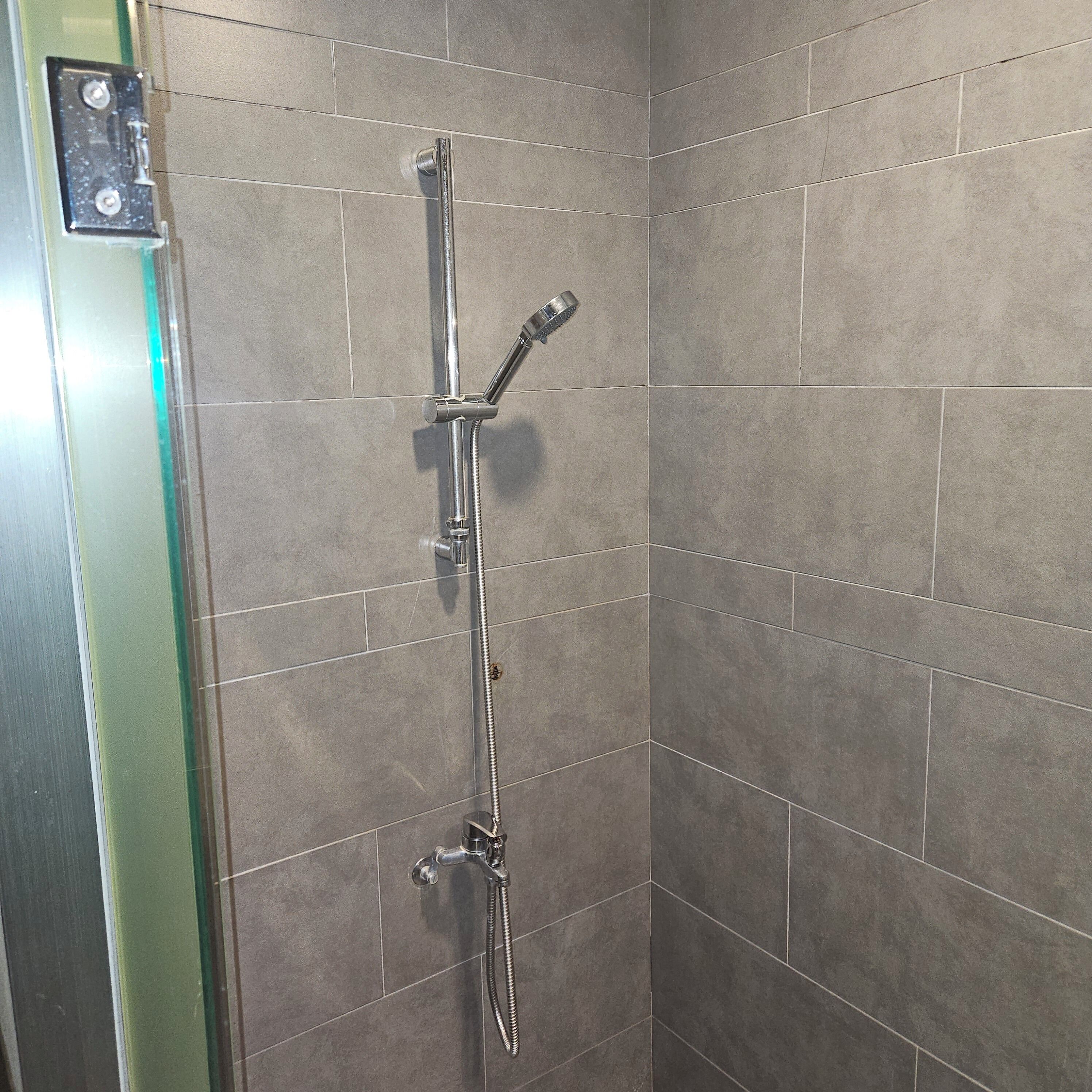 A shower with a handheld showerhead and a fixed showerhead, set in a corner with tiled walls.