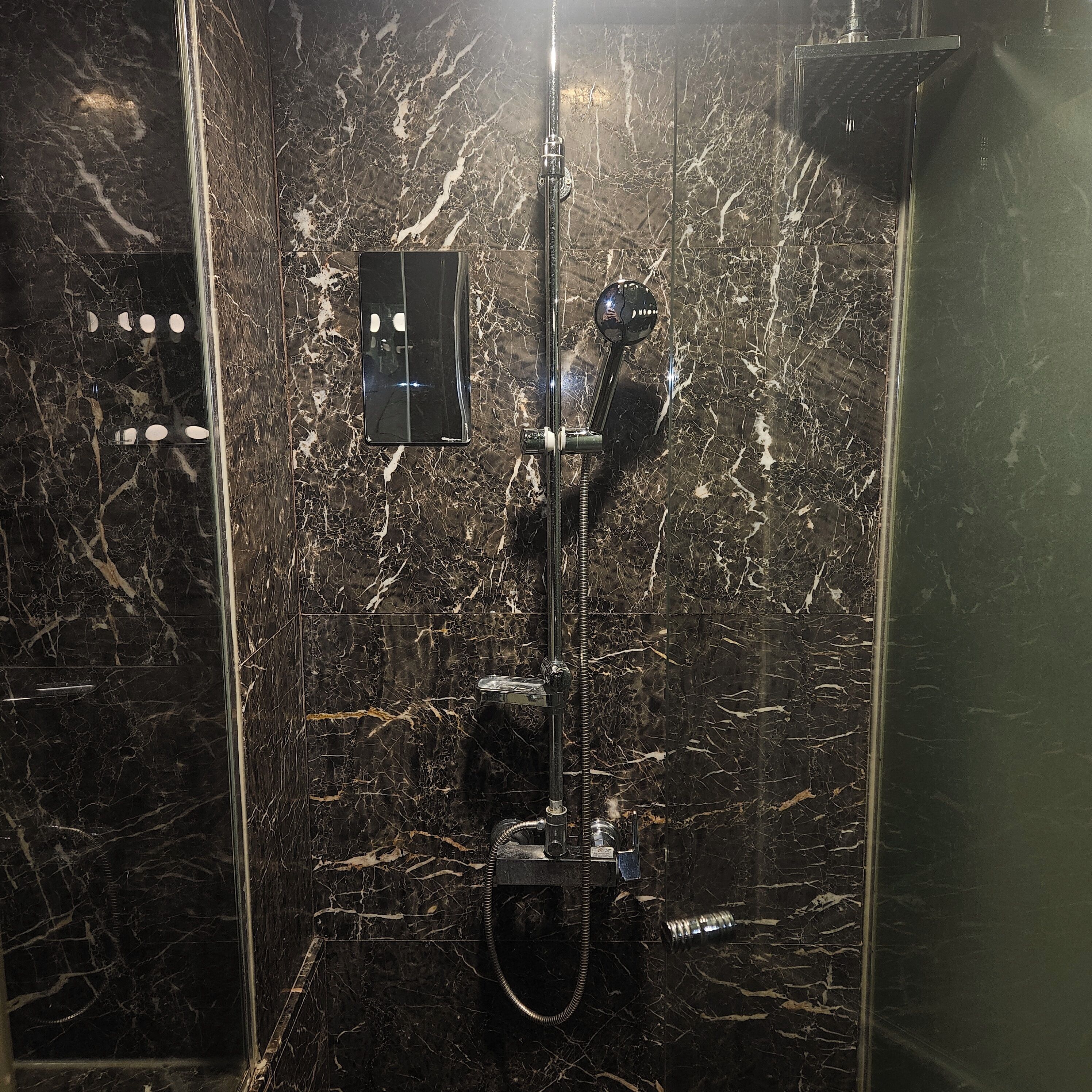 A bathroom with a marble wall, a handheld showerhead, and a control panel.
