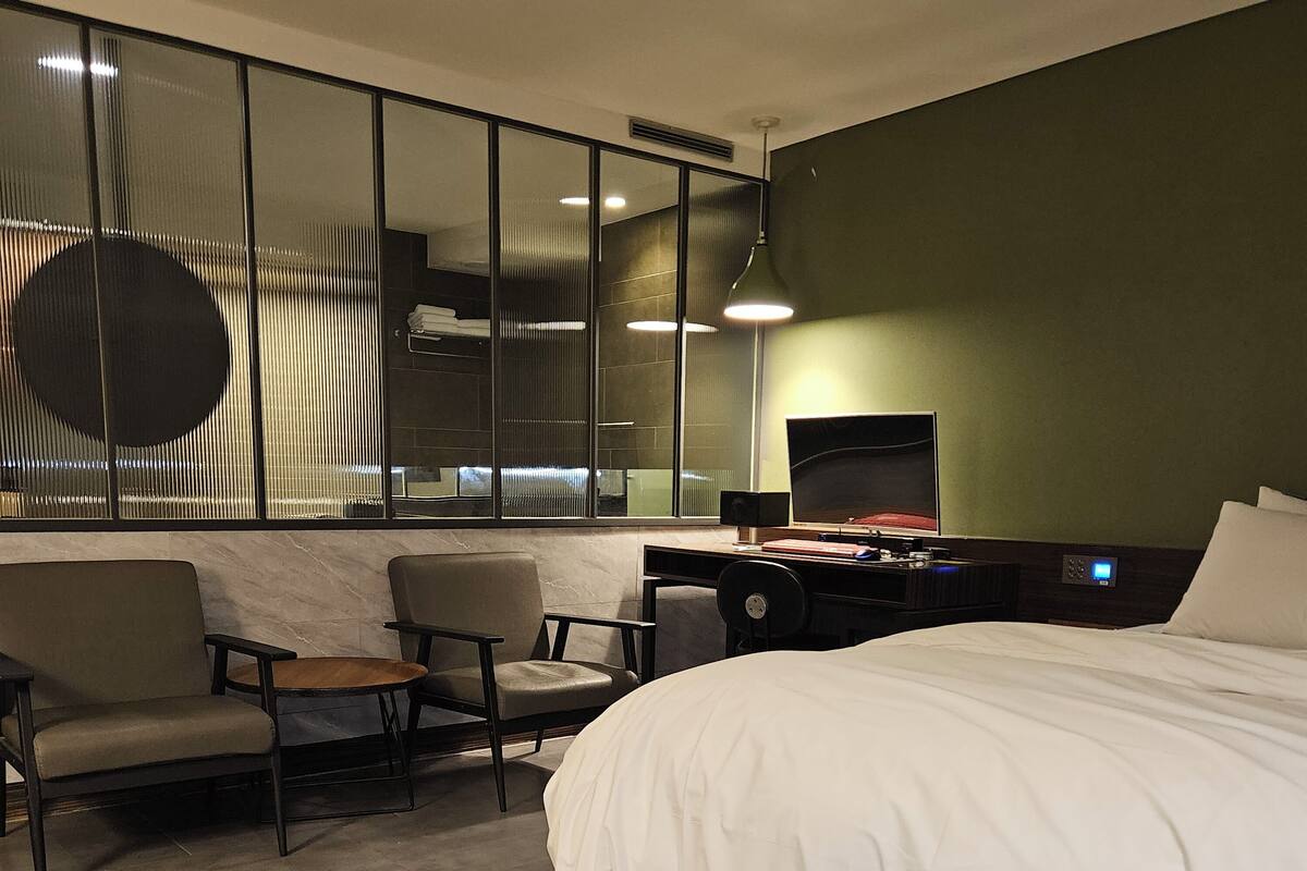 A hotel room with a large bed, a desk with a computer, a chair, and a sofa.