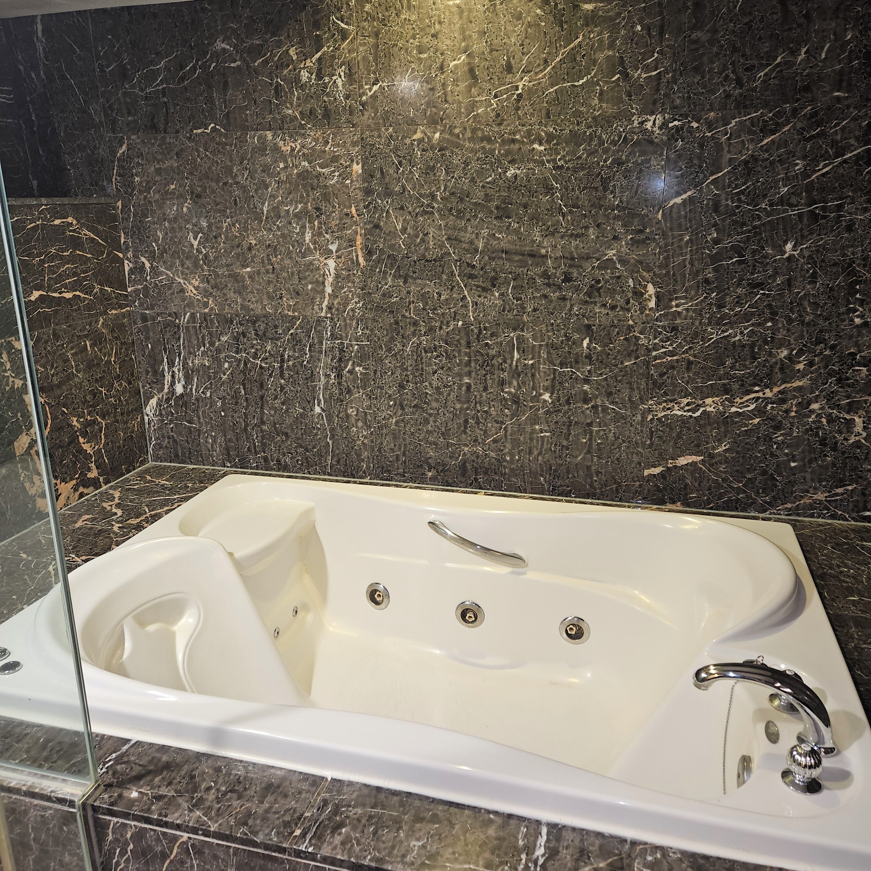 A modern bathroom with a marble wall and a white bathtub.