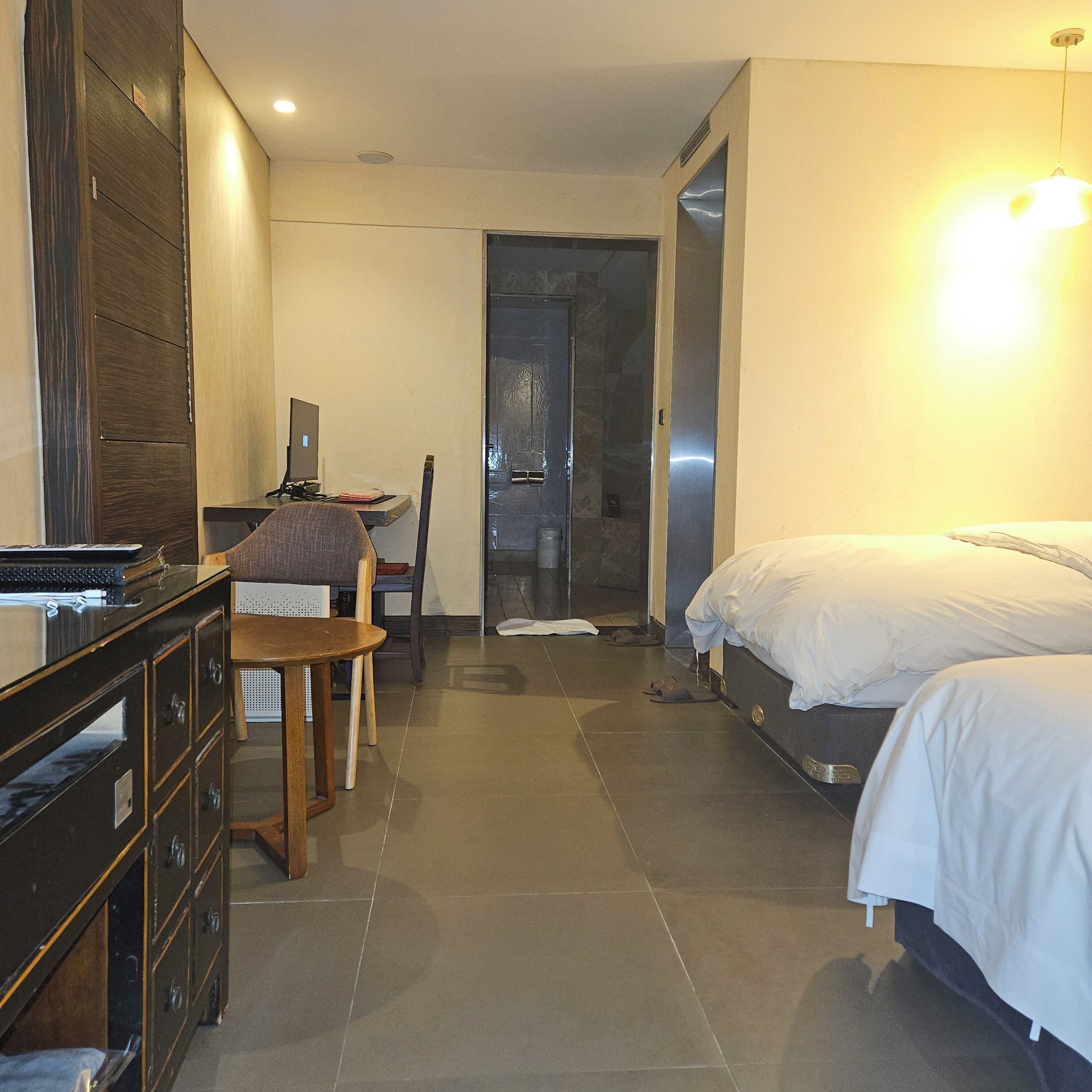 Una habitación de hotel con una cama, un escritorio con una computadora, una silla, un aparador y una puerta que da a un baño.