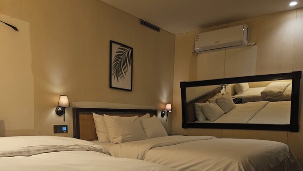 Une chambre d’hôtel avec deux lits, un climatiseur fixé au mur, des lampes de chevet et une œuvre d’art encadrée.