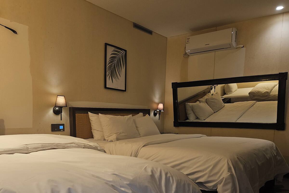 A hotel room with two beds, wall-mounted air conditioning, bedside lamps, and a framed artwork.