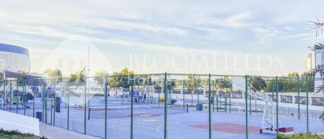 An outdoor basketball court with a fence, surrounded by grass and a paved walkway.