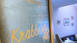 Un comptoir d’accueil doté d’un panneau en verre dépoli sur lequel est inscrit « Bienvenue chez Krabbe » et qui présente le logo de l’entreprise, un crabe.