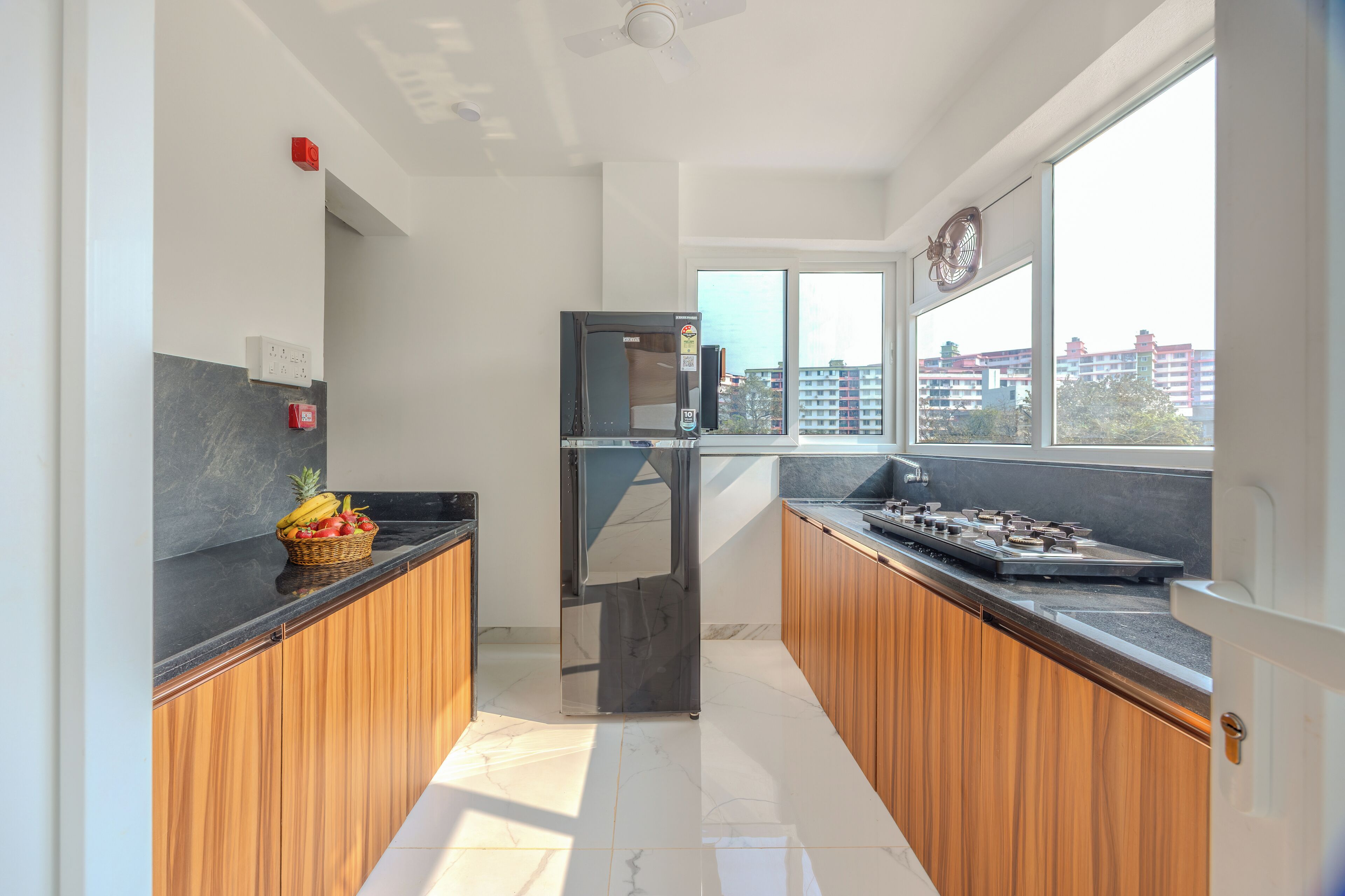 A modern kitchen with wooden cabinets, a stainless steel refrigerator, a built-in stove, and a window offering a city view.