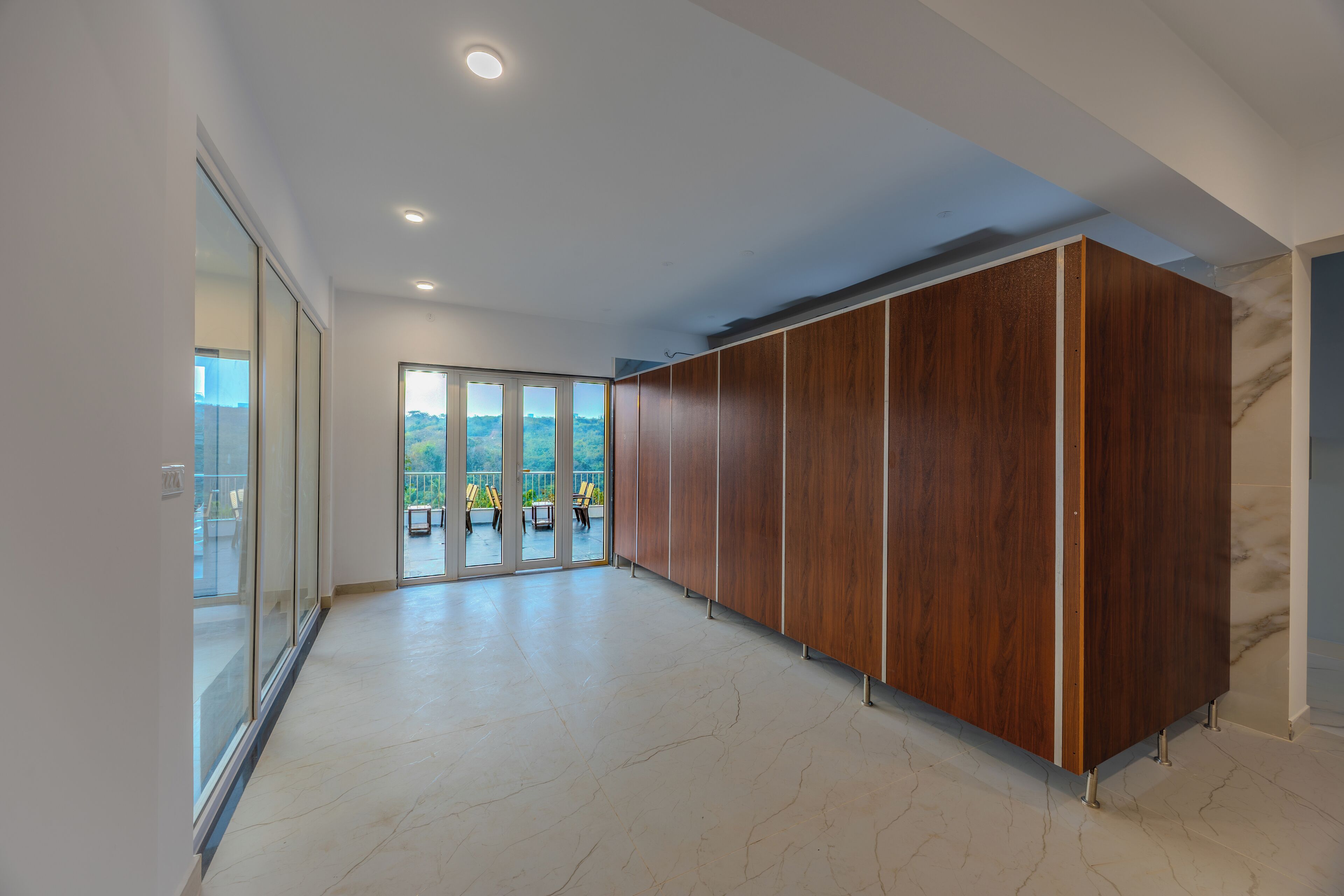 Un pasillo espacioso con un revestimiento de paneles de madera, un vidrio que da a un espacio de estar exterior y un piso de mármol.