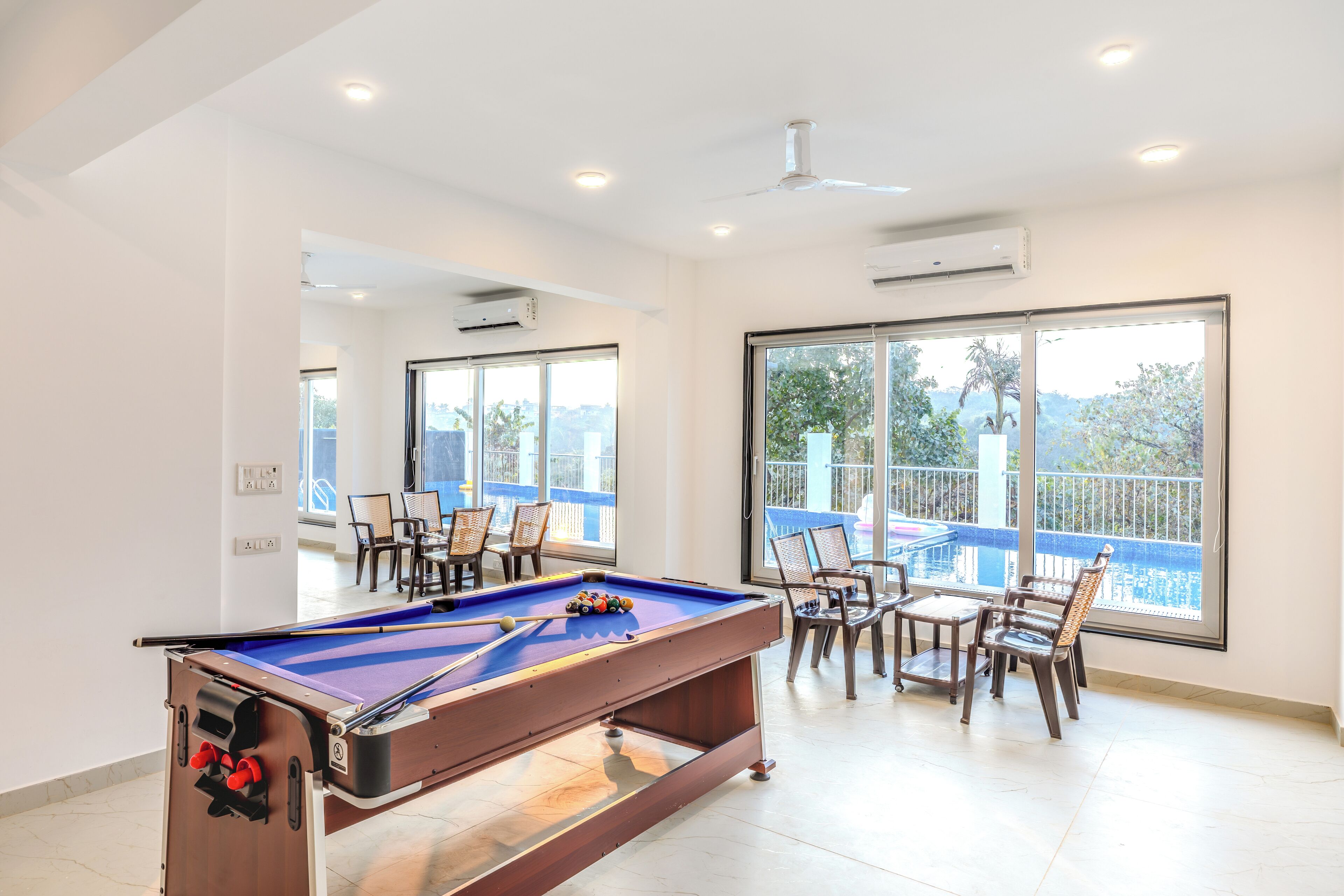 A pool table in a bright room with large windows, a ceiling fan, and a balcony with chairs.