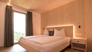 Ein Schlafzimmer mit einem hölzernen Kopfteil, einem Nachttisch, einem Bett mit weißer Bettwäsche und Blick durch ein großes Fenster.