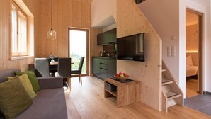 Ein modernes Interieur mit Holzboden, einer Couch, einem Essbereich, einer Küche mit Fernseher und einer Treppe.