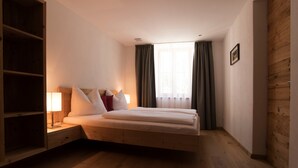 Ein Schlafzimmer mit einem Bett, Nachttischen, einer Lampe, einem Holzschrank und einem Fenster mit Vorhängen.