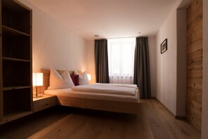 A bedroom with a bed, nightstands, a lamp, a wooden wardrobe, and a window with curtains. - Apartment 'Greiterhof Historika' with Mountain View and Wi-Fi (Lana)