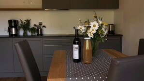 Eine moderne Küche mit Esstisch, Stühlen, einer Kaffeemaschine, einer Weinflasche und einem Blumenstrauß in einer Vase.