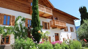Ein zweistöckiges Holzhaus mit Balkonen, einem Garten voller Blumen und blauem Himmel.