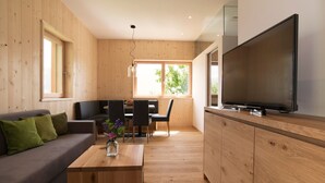 Ein modernes Wohnzimmer mit Holzvertäfelung, einer Couch, einem Esstisch, Stühlen, einem Couchtisch, einem Fernseher und einem großen Fenster.