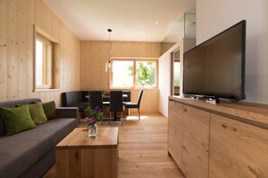 A modern living space with a wooden interior, a sofa, a dining table, chairs, a coffee table, a TV, and a large window. - Apartment 'Greiterhof Weingarten' with Mountain View and Wi-Fi (Lana)