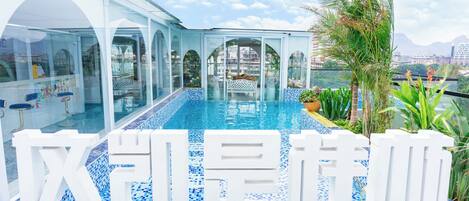 A modern hotel with a large glass-enclosed pool, outdoor seating, and tropical plants.