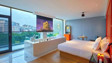 Una camera d'albergo moderna con un letto grande, una toeletta con specchio, un piccolo tavolino e un'ampia finestra che offre vista sulla città.