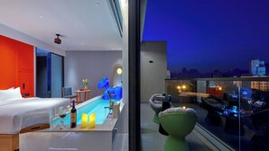 Una habitación de hotel moderna con cama, una piscina pequeña y un balcón con vista a la ciudad y las montañas.