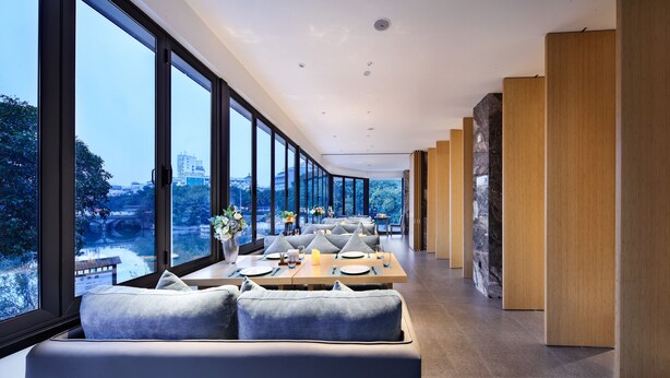 Un comedor moderno con ventanas amplias, una mesa larga con asientos y vistas a un paisaje urbano.