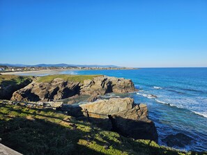 A coastal landscape with rocky cliffs, a beach, and a distant town. - Casa César 1 km from the famous Playa de las Catedrales in Lugo. (San Miguel de Reinante. Barreiros)