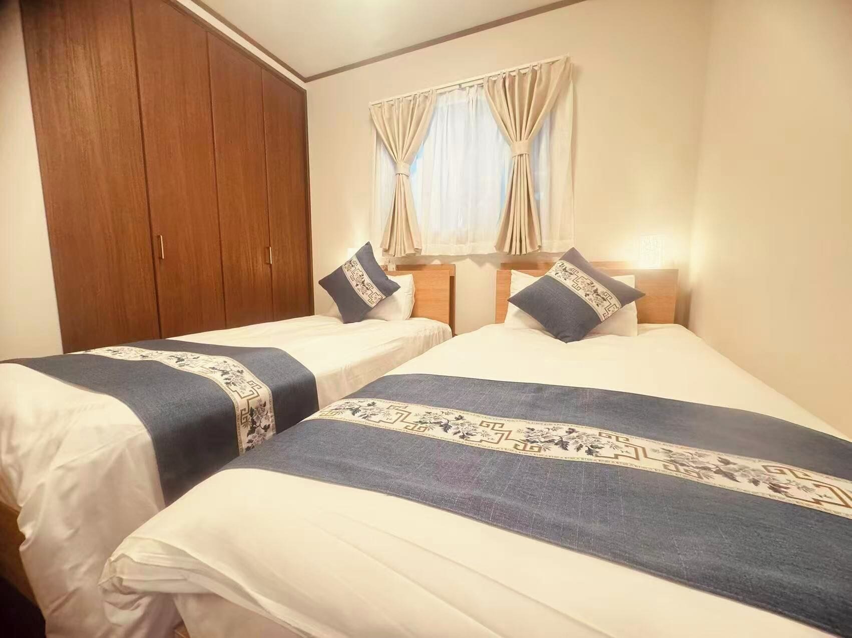A hotel room with two beds, a wardrobe, and a window with curtains.