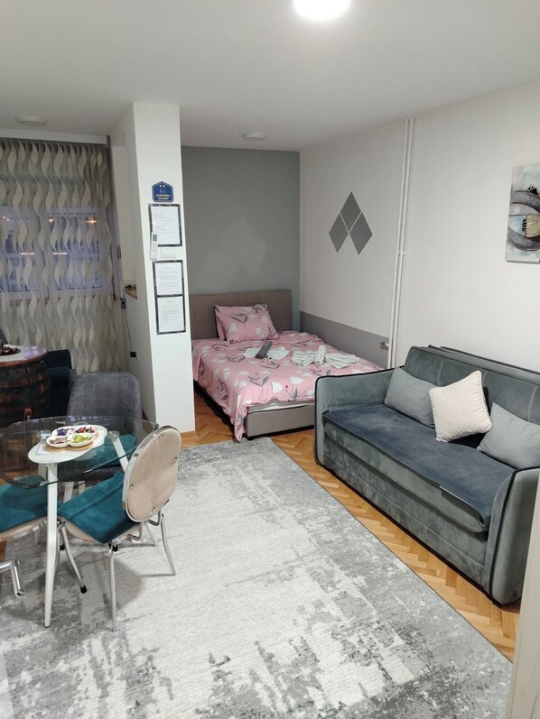 A compact living space with a bed, a sofa, a small table with a chair, and a decorative wall.