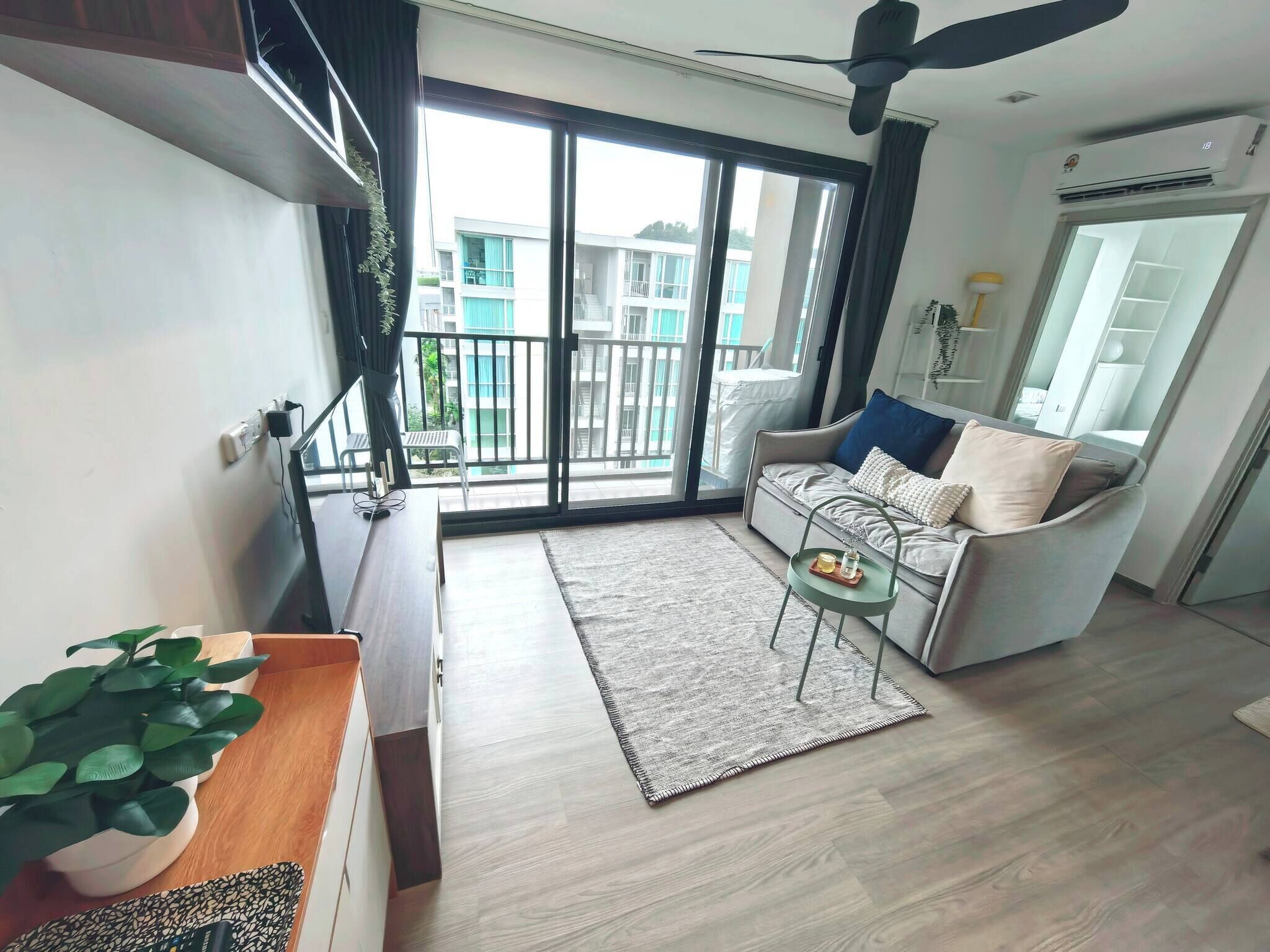 A modern living room with a sofa, a coffee table, a plant, and a balcony with a view of buildings.