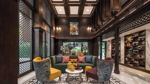 Een ruime lobby met een grote groene bank, twee gestreept fauteuils, een bijzettafeltje en een boekenplank vol boeken en decoratieve objecten.