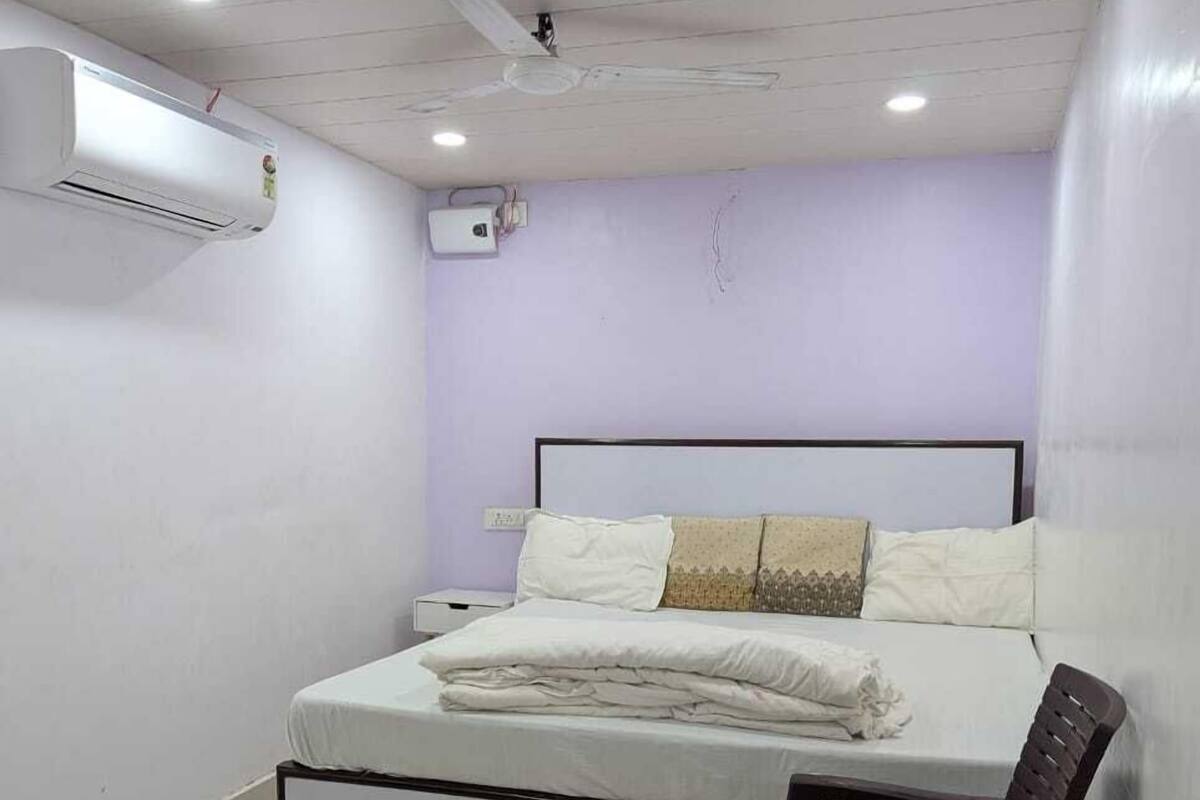 Un dormitorio con una cama, una silla, un equipo de aire acondicionado y un ventilador de techo.