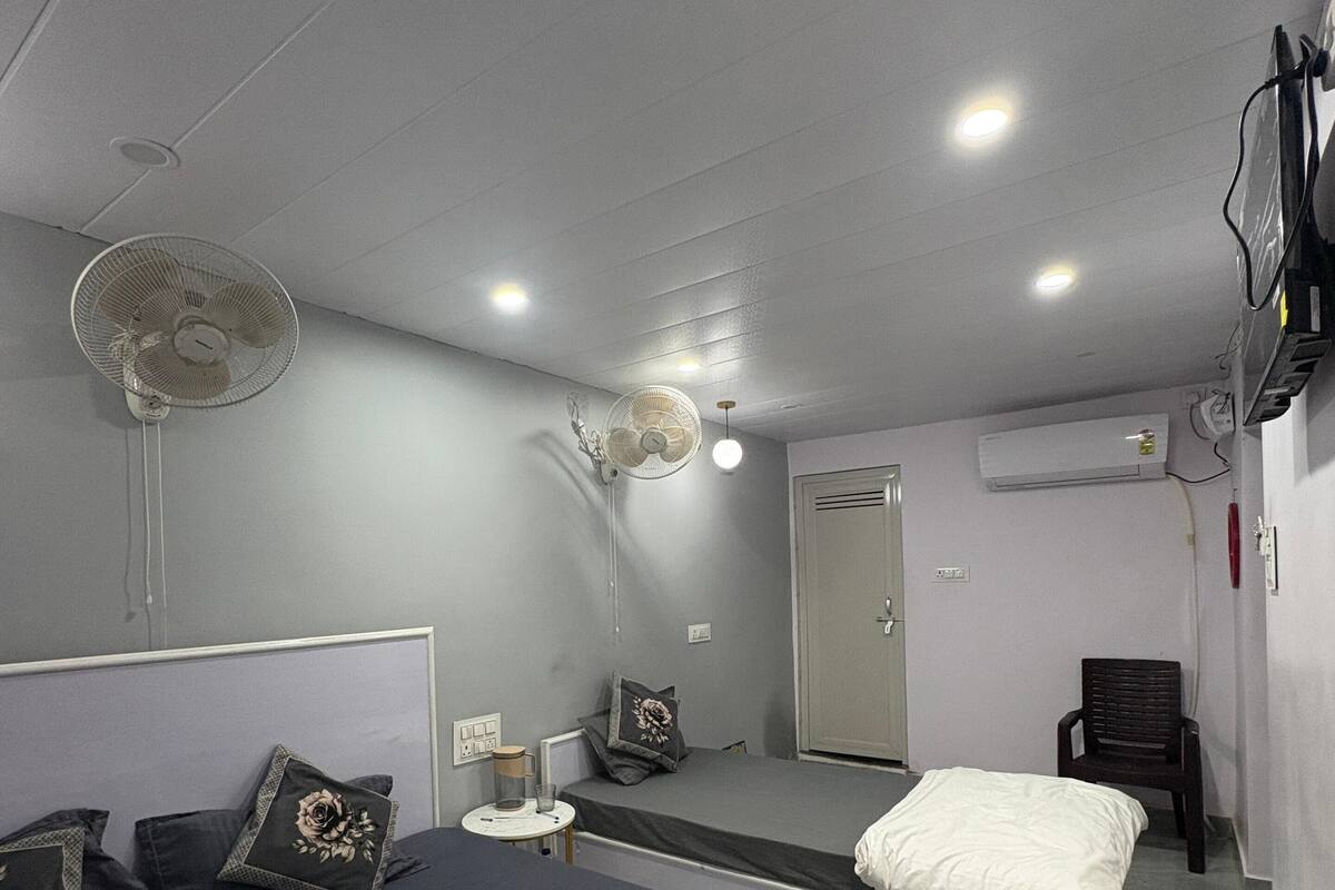 Una habitación de hotel con dos camas, un ventilador de techo, un equipo de aire acondicionado y una mesita con lámpara.