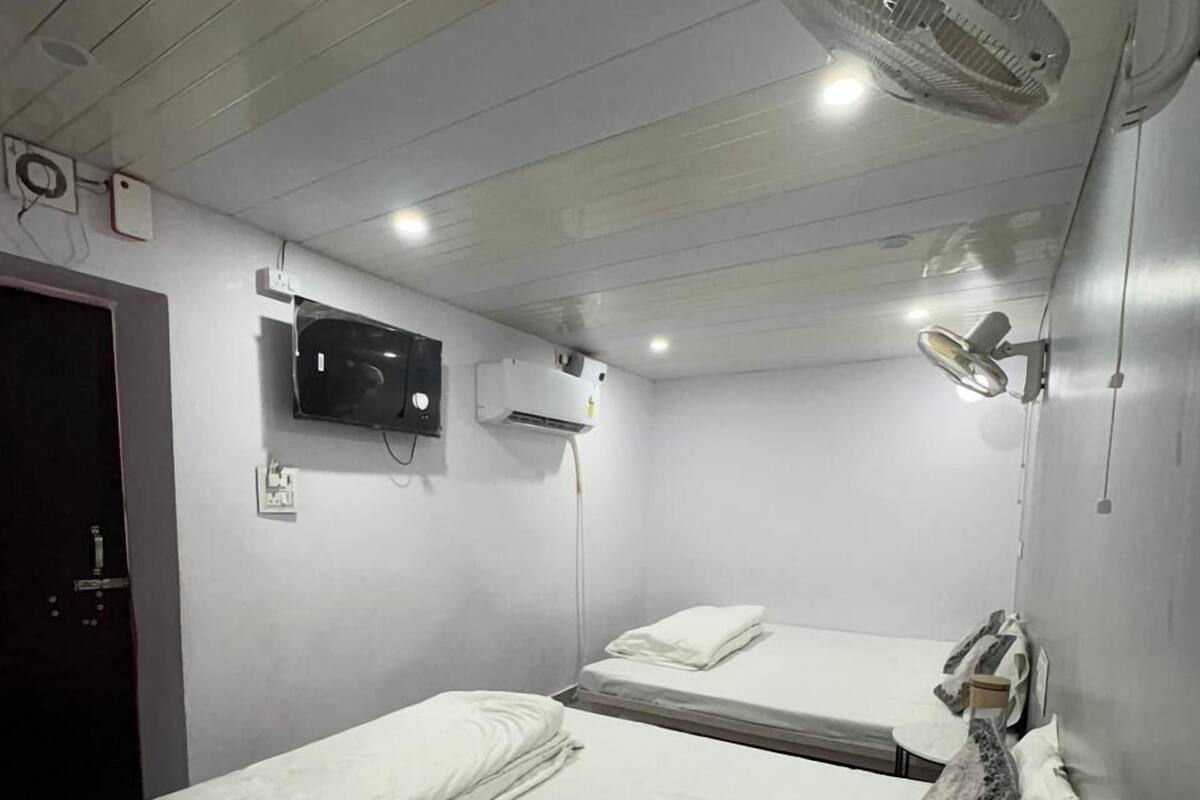 Una habitación de hotel con dos camas, televisor, aire acondicionado y ventilador de techo.