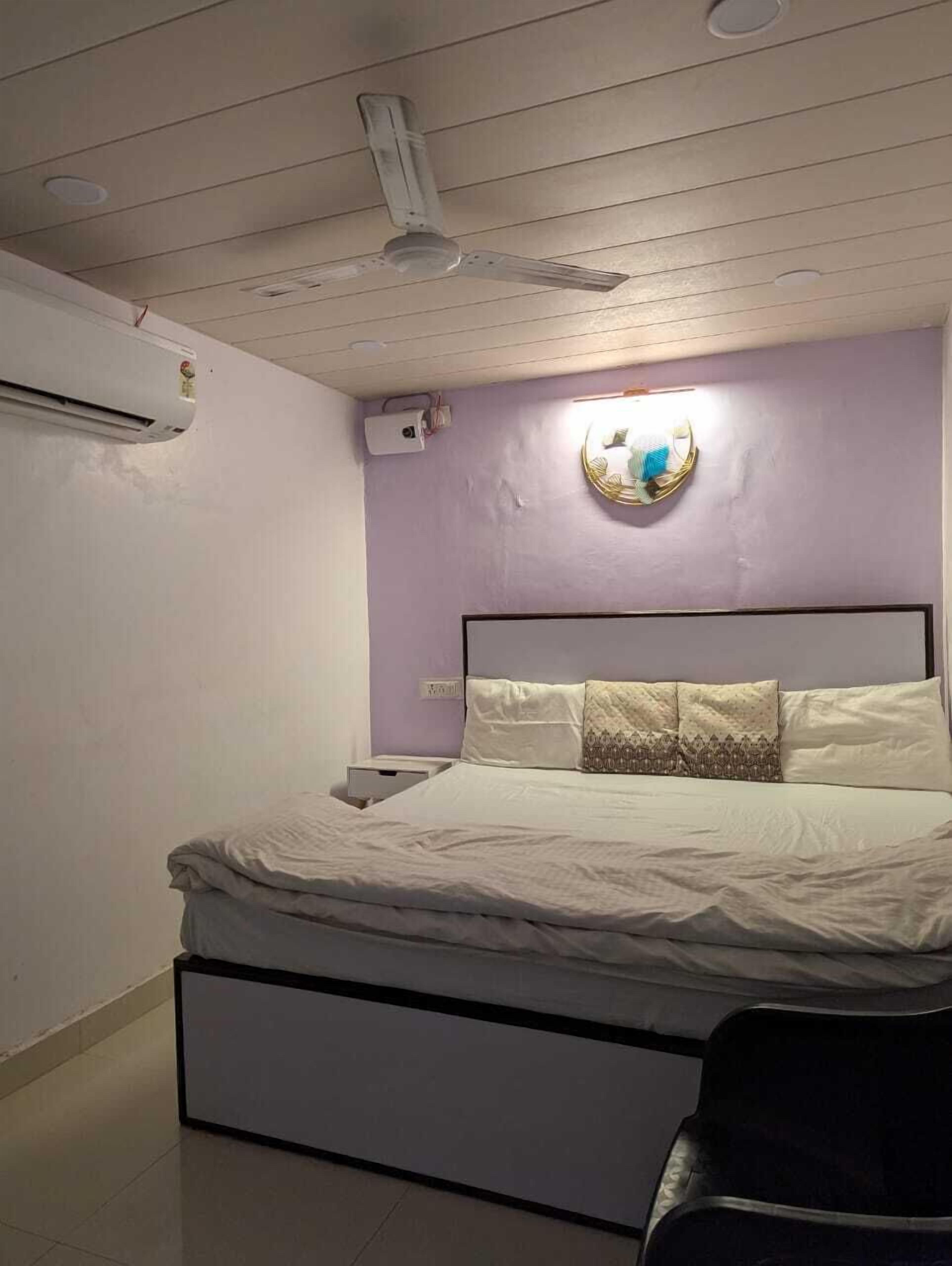 Une chambre à coucher comprenant un lit, un climatiseur, un ventilateur de plafond et un luminaire fixé au mur.