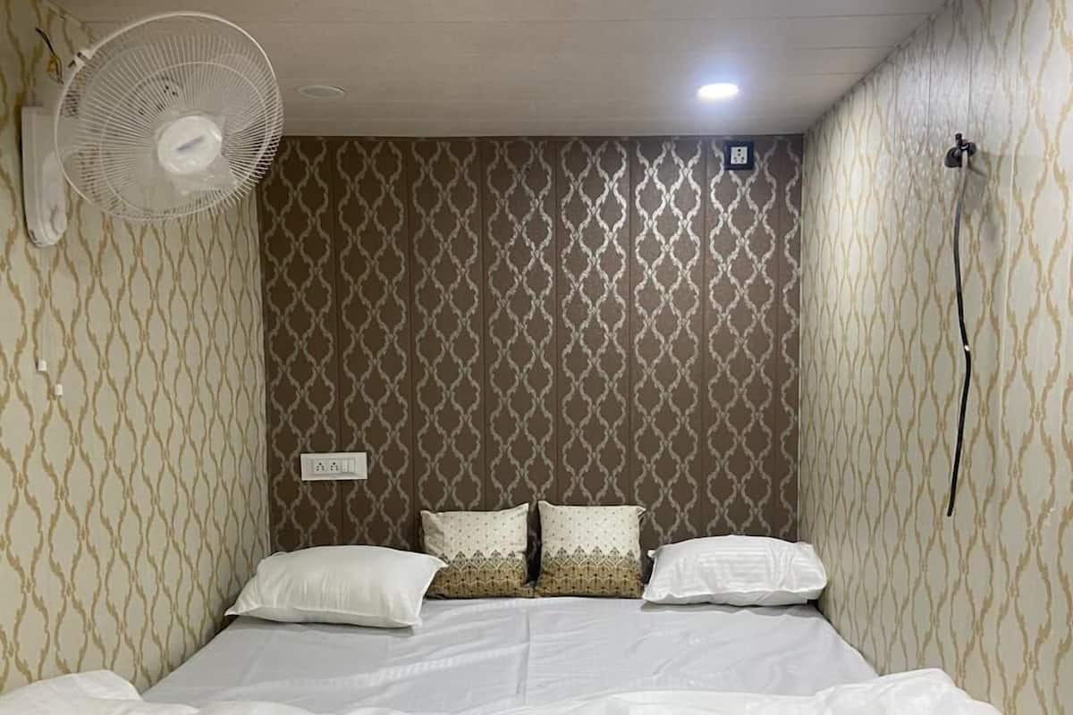 Una cama bien hecha con ropa de cama blanca, un ventilador de pared y un papel tapiz estampado.