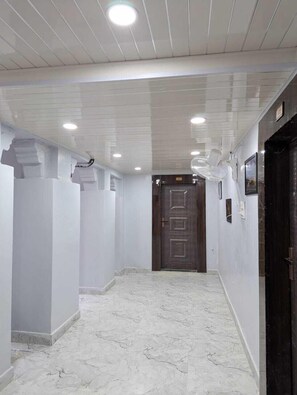Un pasillo con suelo de mármol, paredes blancas y una puerta de madera oscura al final.