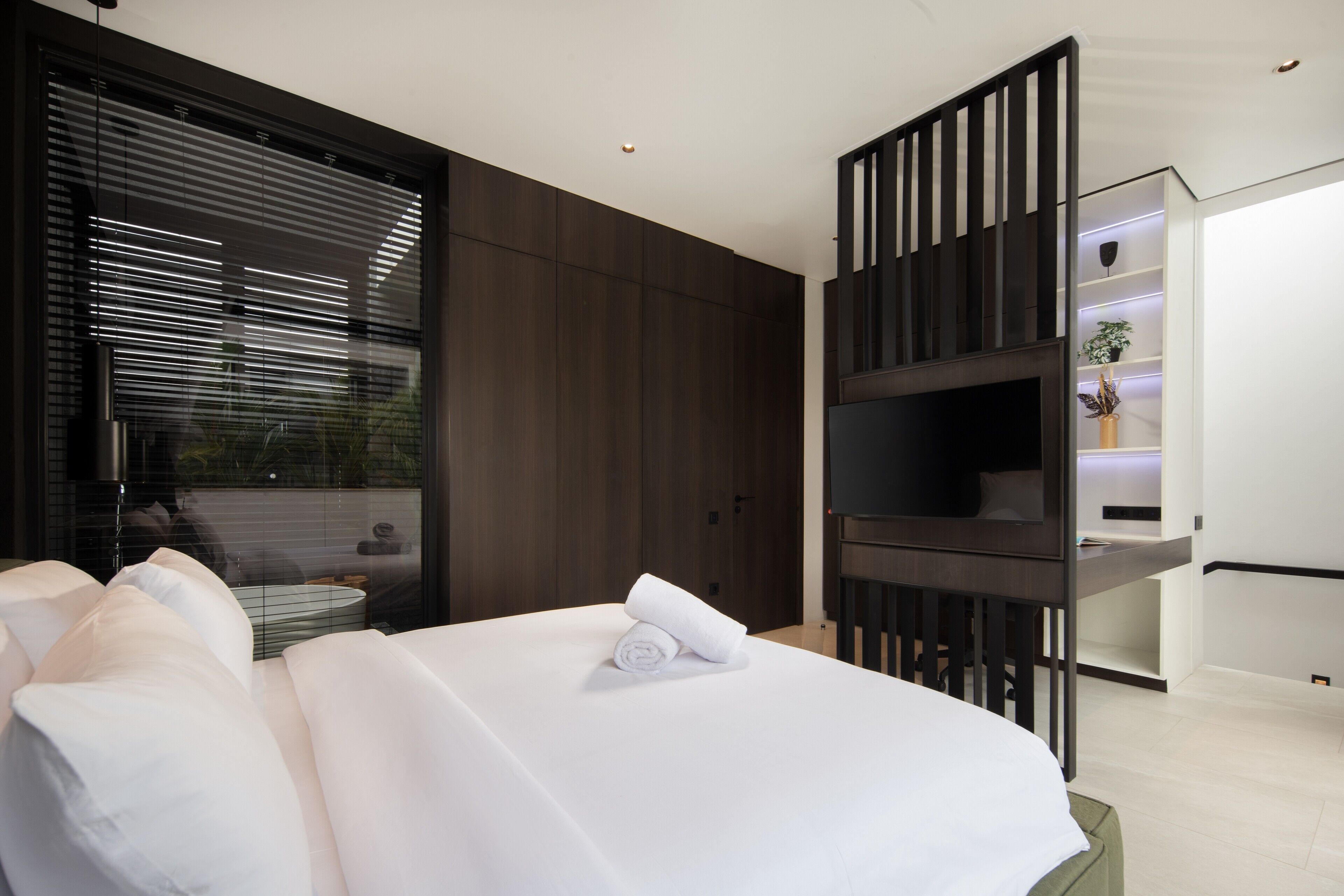 A modern hotel room with a large bed, dark wood paneling, a TV, and a small seating area with a table and chairs.
