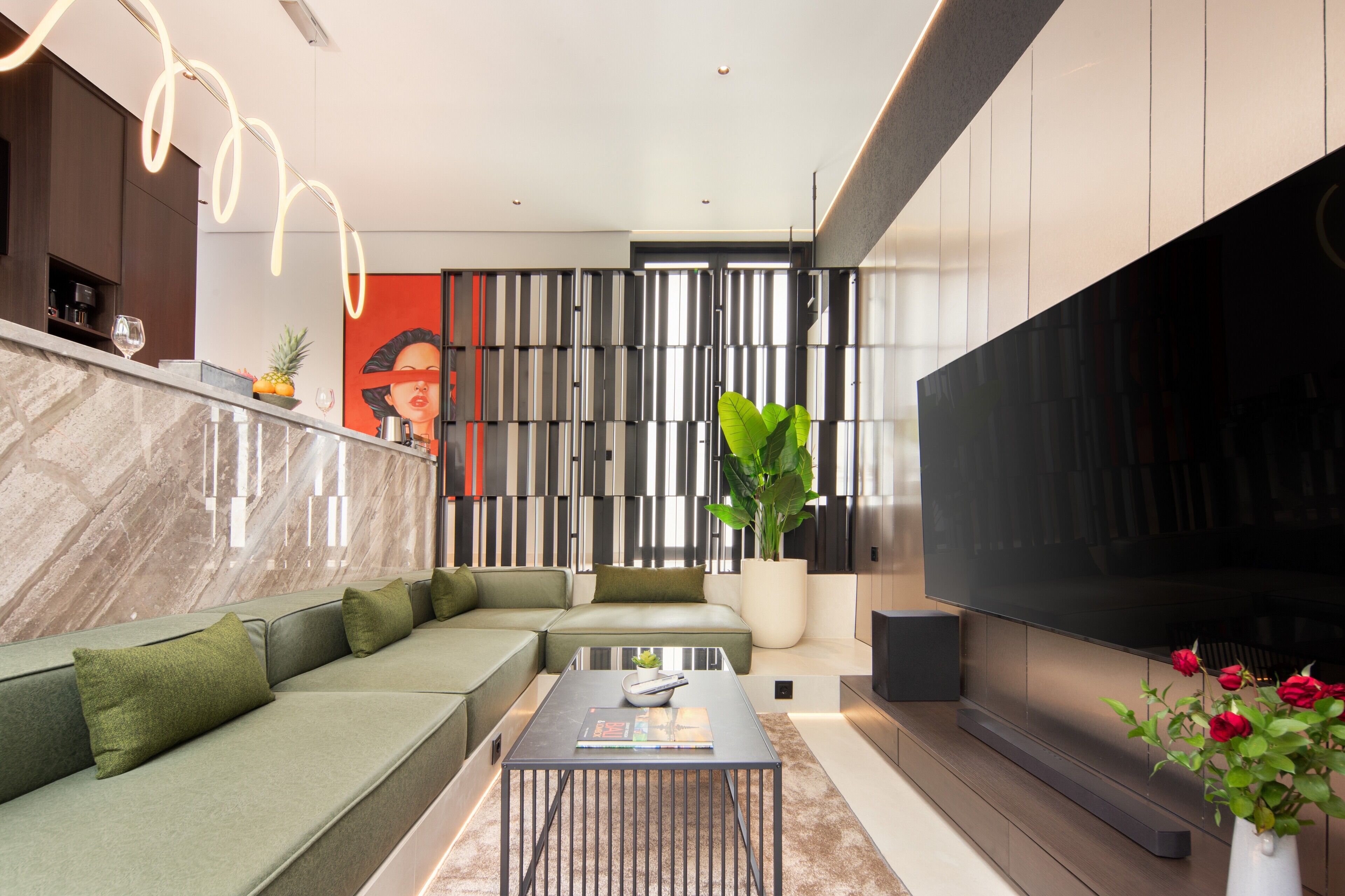 Un salon moderne avec un canapé d’angle, une table basse, un téléviseur à écran plat et une grande plante en pot.