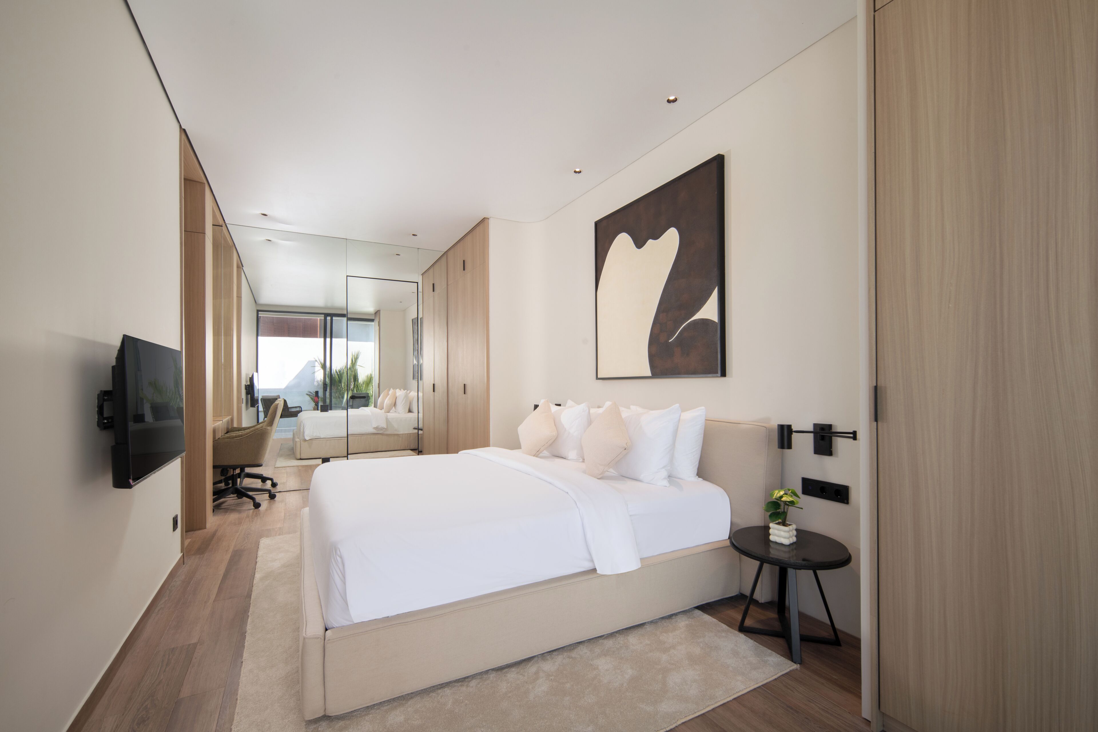 Un dormitorio moderno con una cama grande, un televisor de pantalla plana, un escritorio y un espejo amplio.