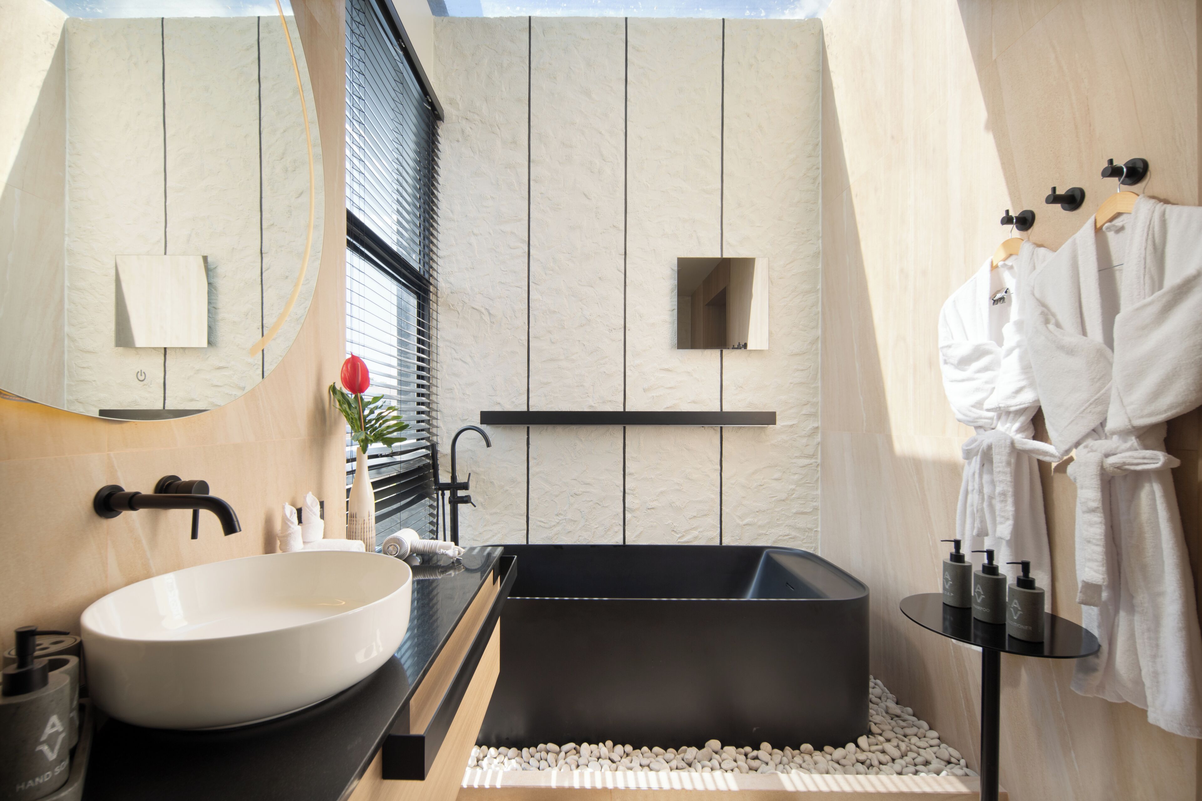 A modern bathroom with a large white sink, a black bathtub, and a small window with blinds.