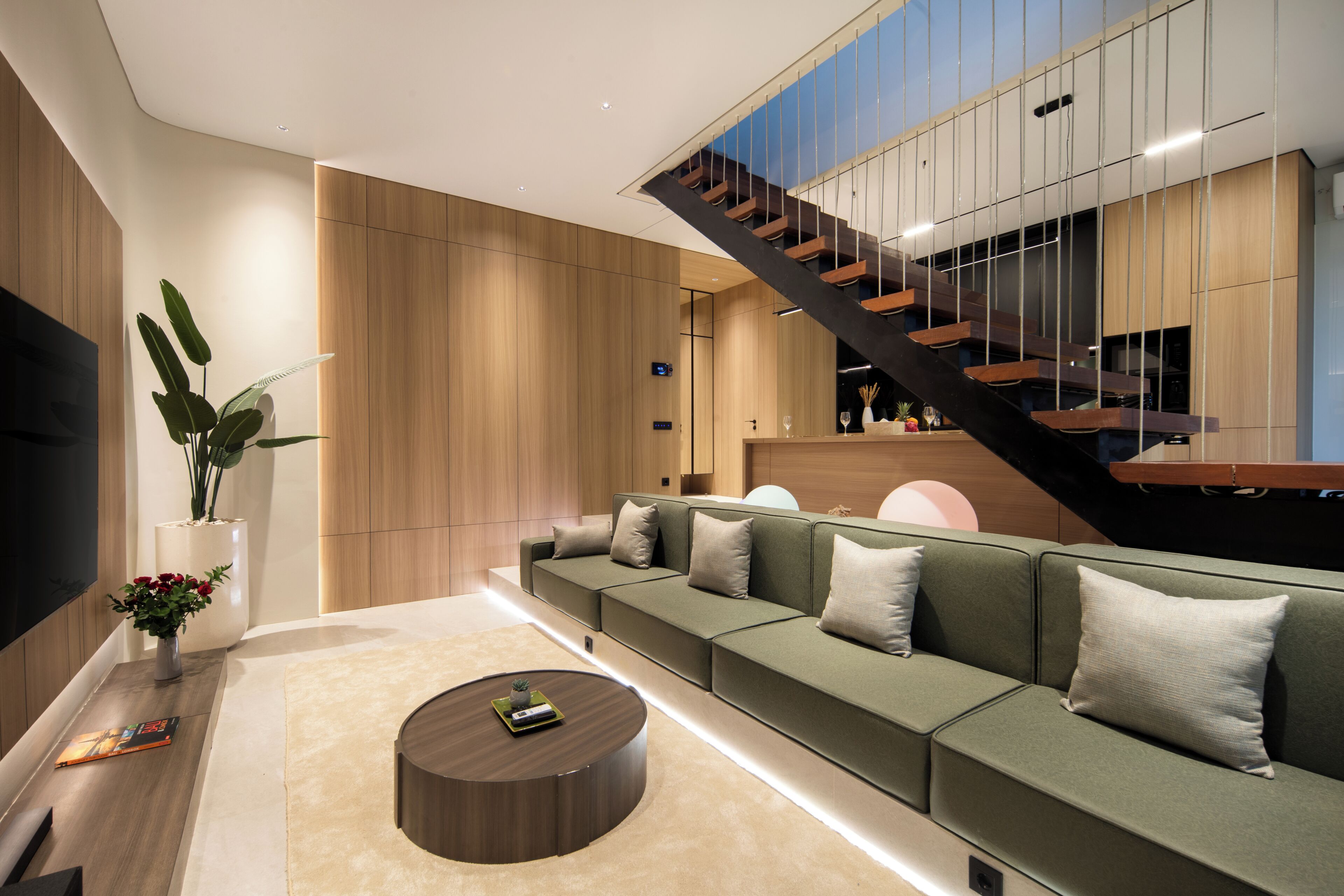 Un salon moderne avec un canapé vert, une table basse en bois et un escalier doté d’une rambarde en verre.