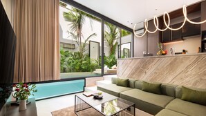 Una sala de estar moderna con un sofá, una mesa de centro y vistas a una piscina y vegetación al exterior.