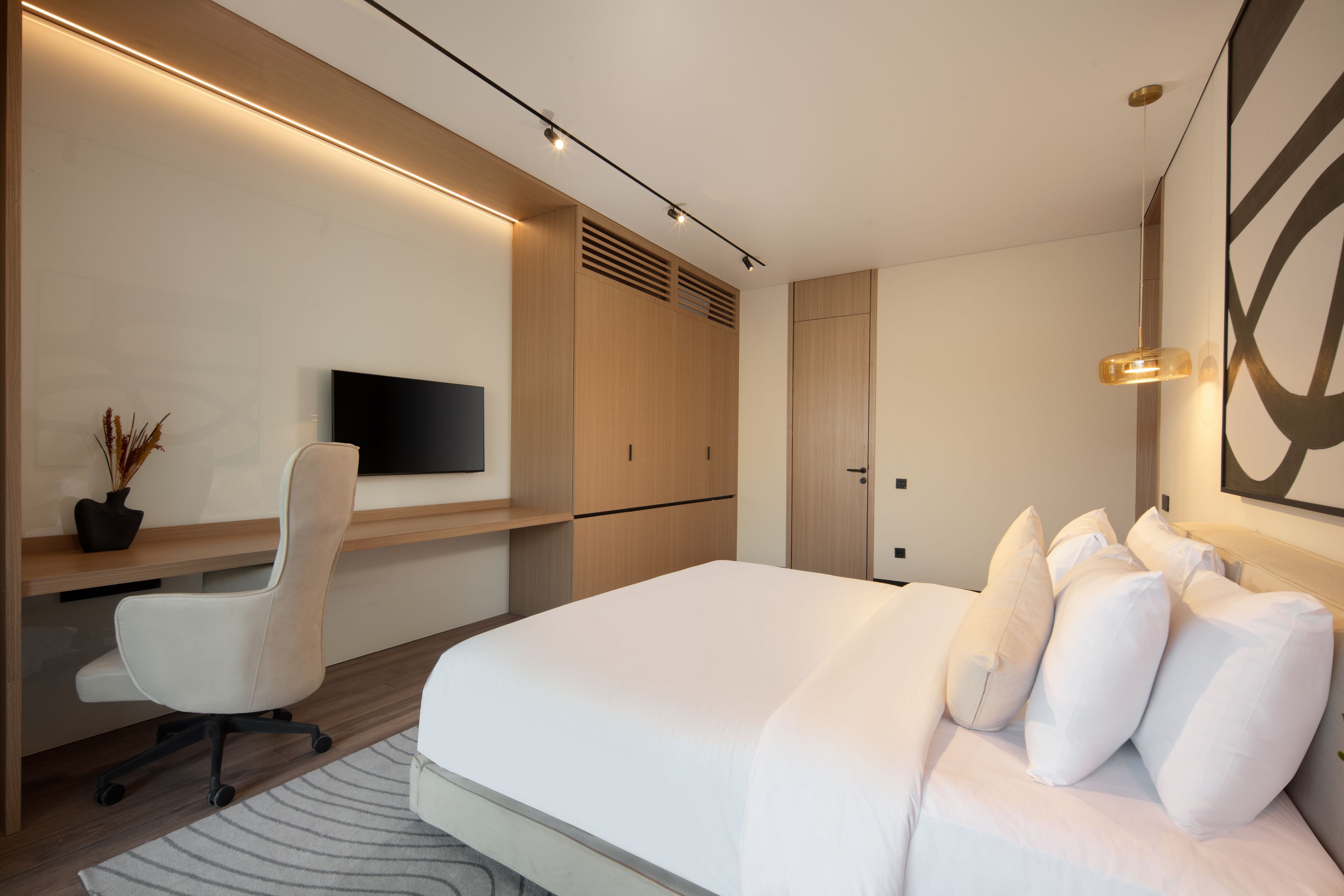 Une chambre d’hôtel moderne dotée d’un grand lit, d’un bureau avec une chaise, d’un téléviseur à écran plat et d’une œuvre d’art accrochée au mur.