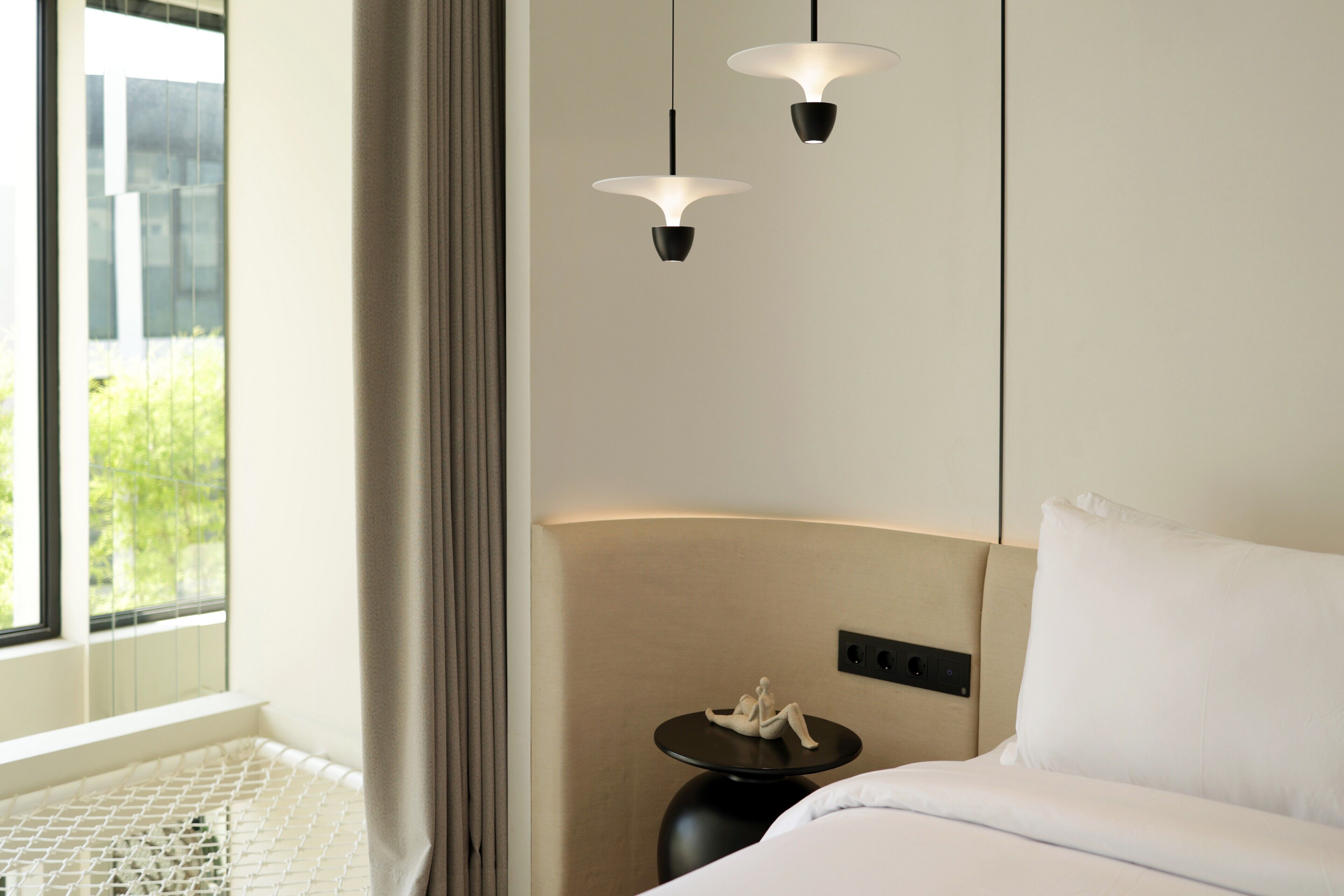 A hotel room with a bed, a small round table with a lamp, and a window with curtains.