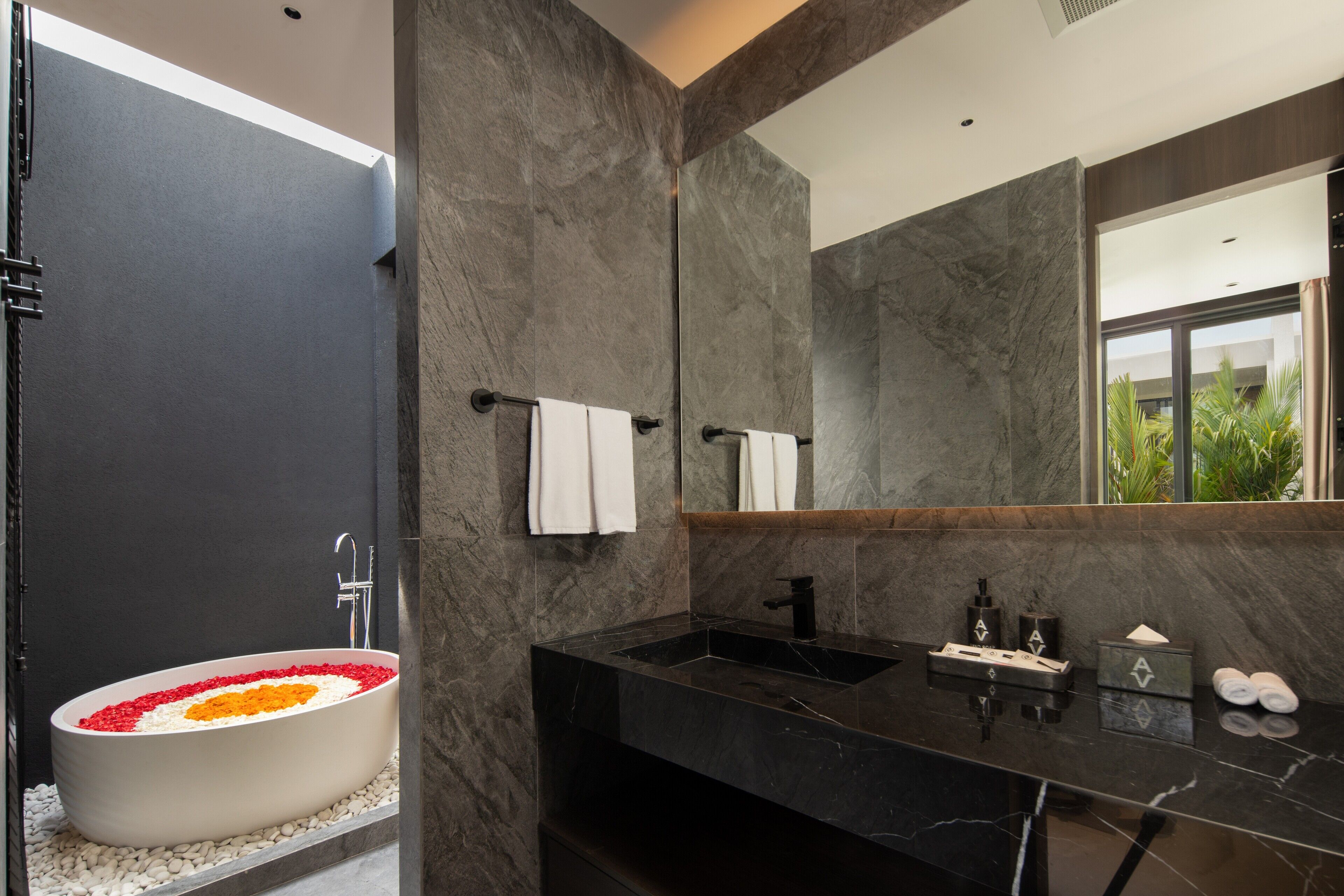 A modern bathroom with a large oval sink, a mirror, and a bathtub with flower petals.